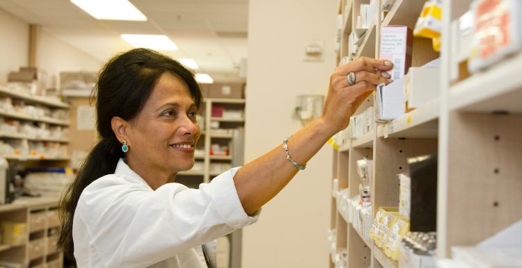 A pharmacist taking a box of medication off a shelf. 
