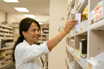 A pharmacist taking a box of medication off a shelf. 