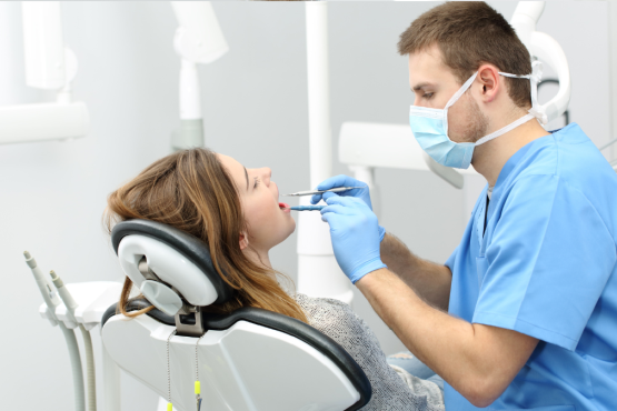 A male dentist wearing a face mask giving dental treatment to a female patient. 